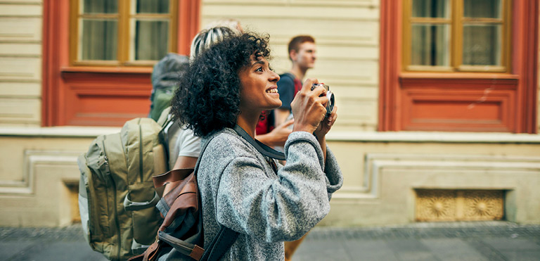 Woman wearing backpack holding a camera taking a photo in a street