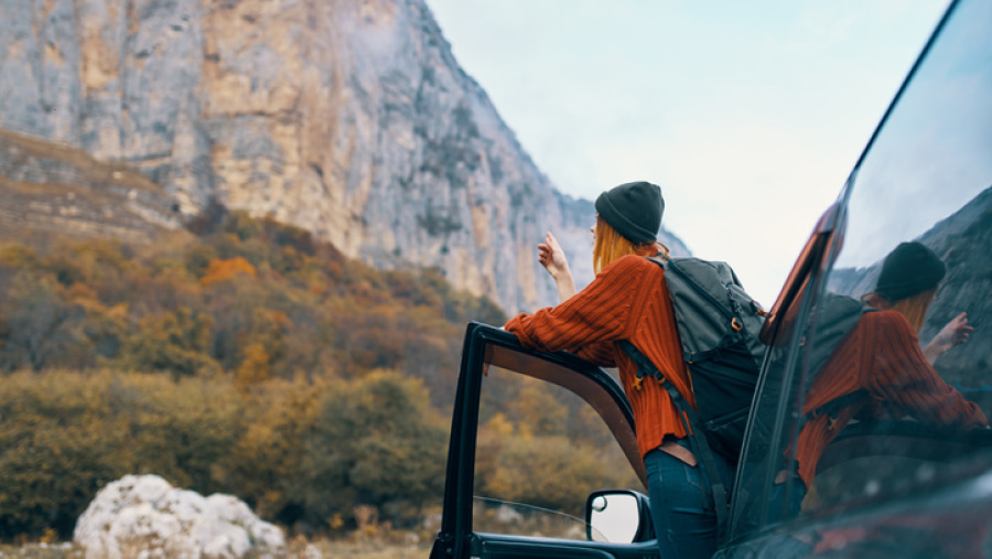 A person leaning out of a vehicle on its open door looking at the surrounding mountainous landscape