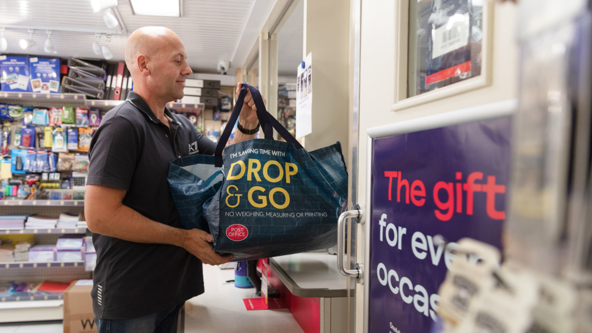 Male customer holding a drop and go bag ready to hand over a counter at a Post Office branch