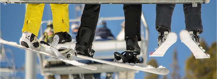 Skier legs and boots in skis on a ski lift with other ski lifts with skiers in them in background