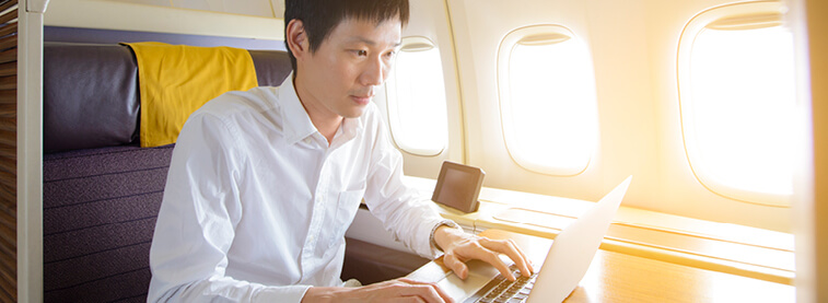 Man on plane in upgraded seating working on his laptop