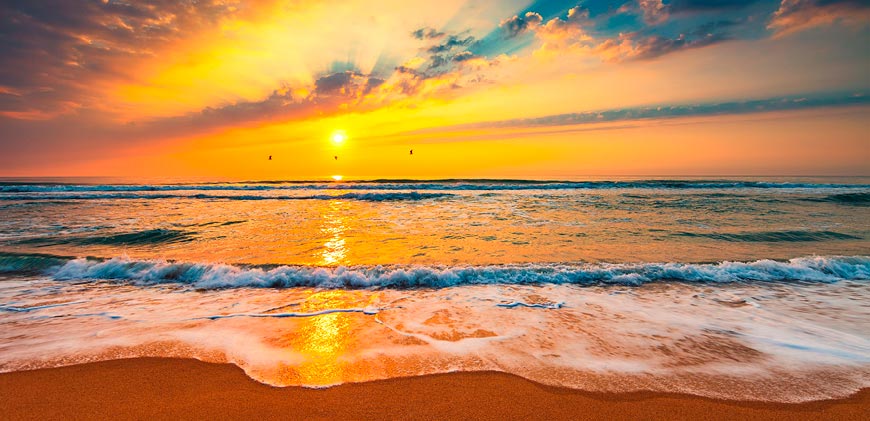 Beach with sea waves lapping on to beach and a beautiful sunset in the distance