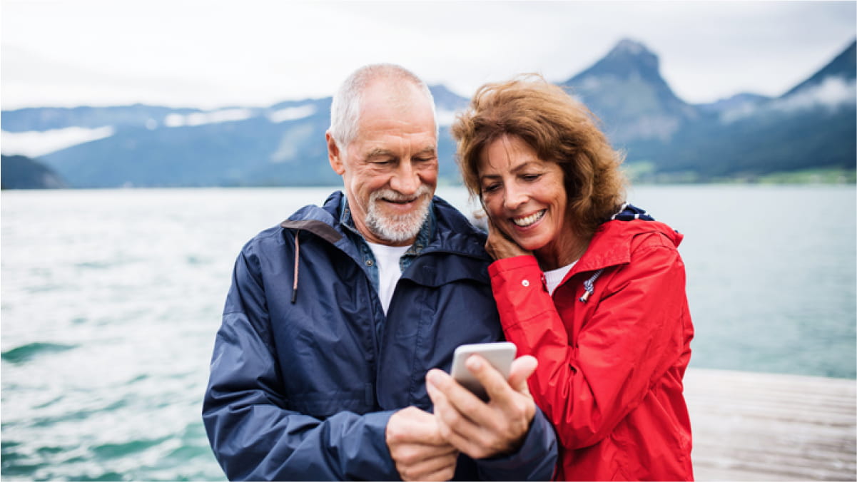Elderly couple smiling both looking at mobile phone held by the male