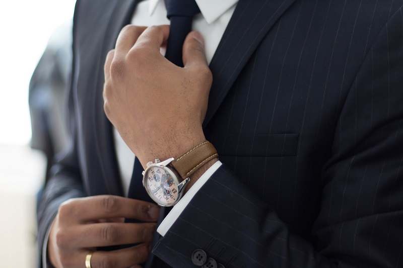 Close up of man wearing smart watch and suit adjusting his tie