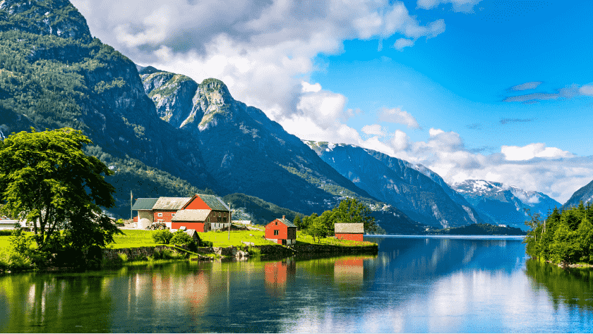 Scenic view of a river under a blue sky, surrounded by mountains and trees, houses in the foreground