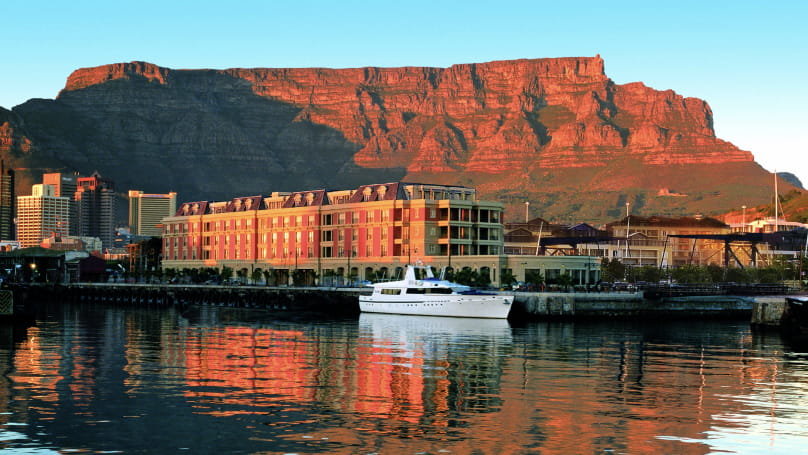 A white cruiser sits in the sunset-lit waters of Cape Town harbour, with the famous Table Mountain in the background
