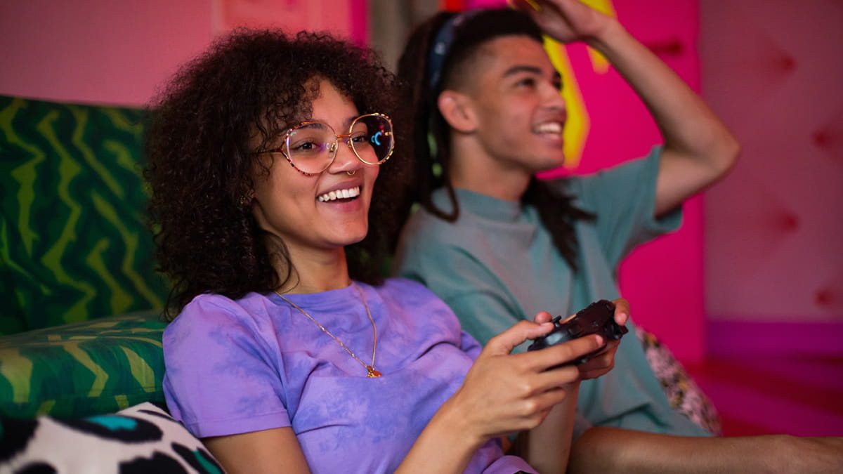 Girl and boy sitting down, girl with gaming controller in her hand playing games