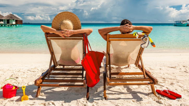 a couple sitting on sun loungers on a tropical beach