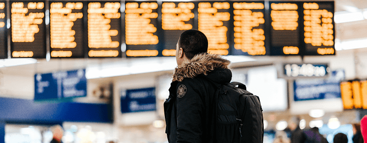 Male wearing winter jacket and backpack looking up at departures board