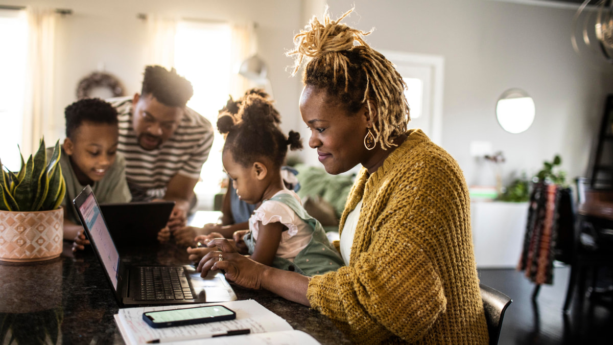 A family of four sitting at the table, while the mother, father and son are looking at the laptop