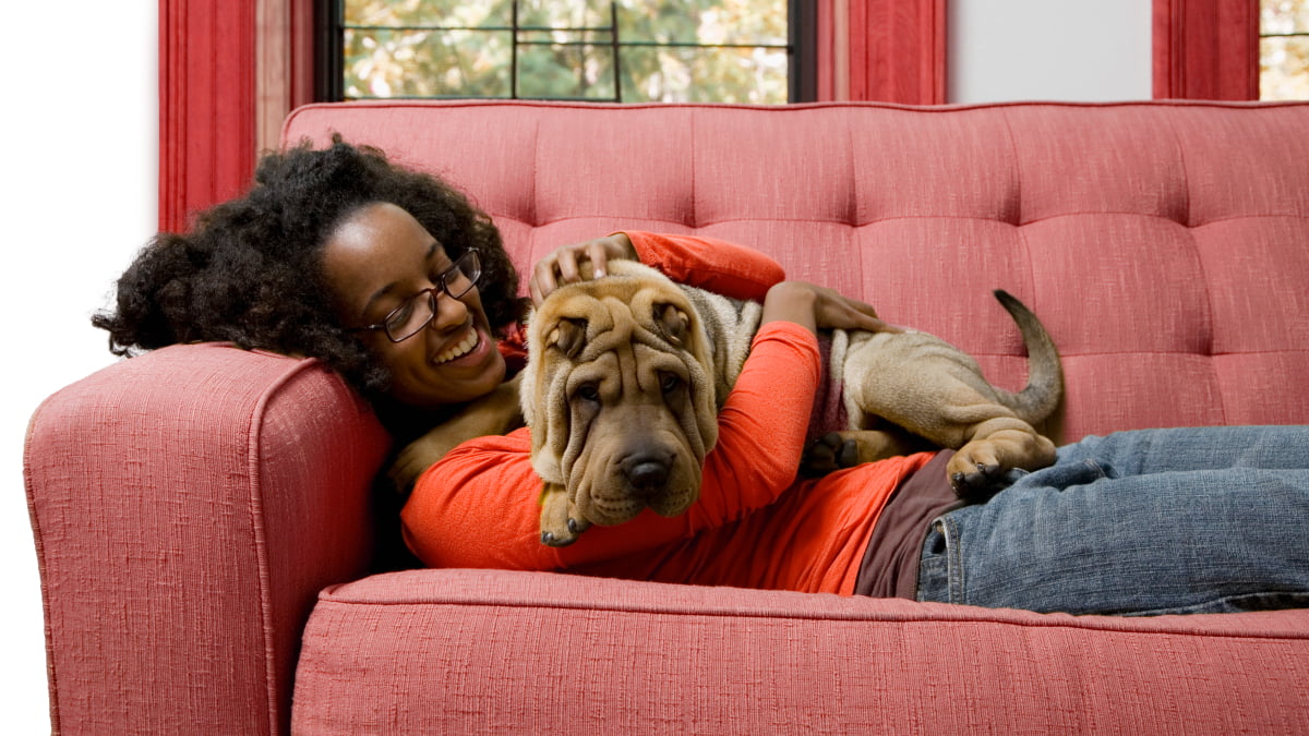 A smiling young woman laying on a couch cuddling her pet dog
