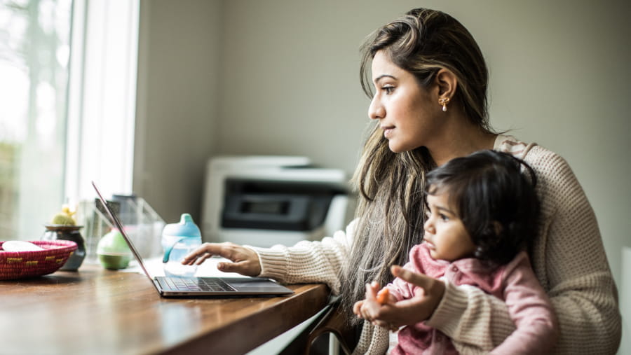 Mother holding baby in one arm while typing on the laptop with other hand