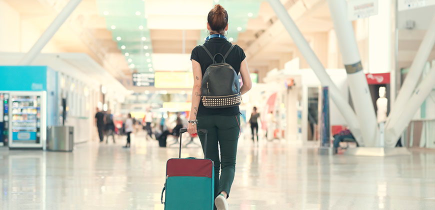 Woman wearing backpack walking at the airport pulling wheeled luggage behind her