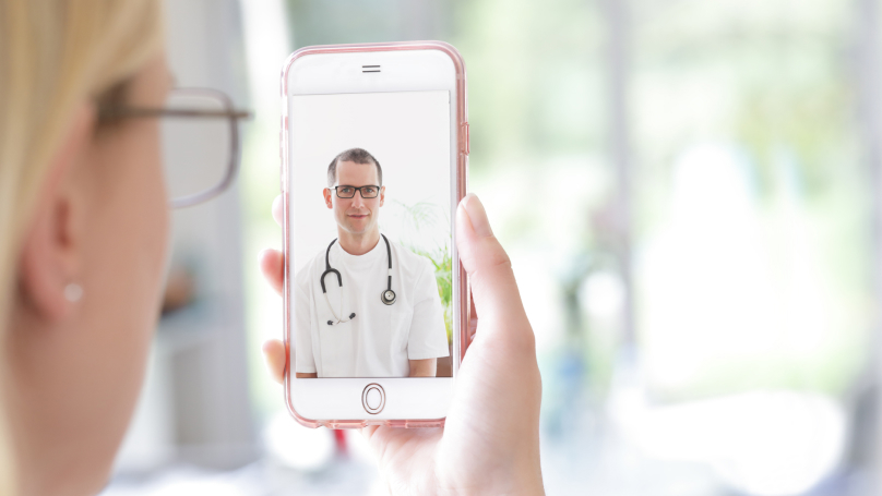 Woman holding up mobile phone, showing a doctor on the screen