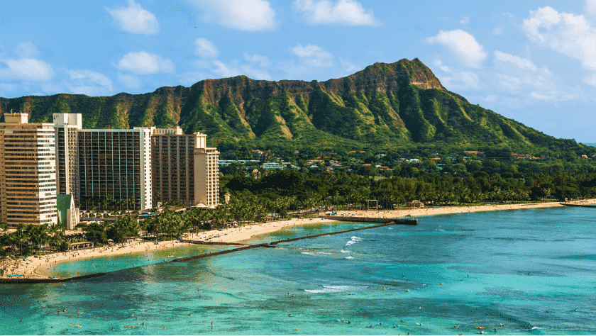 Coastline city buildings with mountains in the background and clear blue sea in the foreground