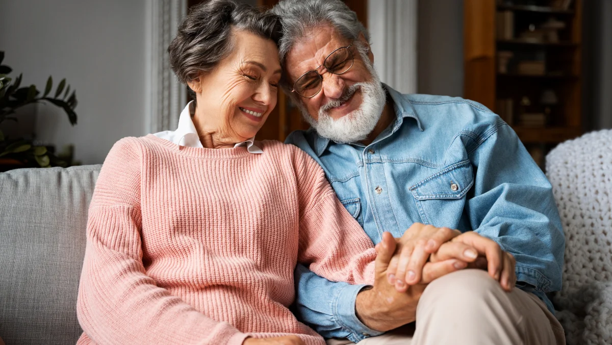 an older couple seated on a sofa holding hands and smiling