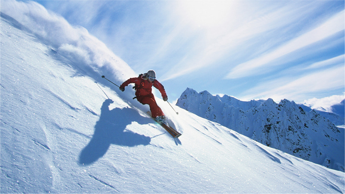 A person wearing red ski gear and holding ski poles skiing on a slope in the mountains