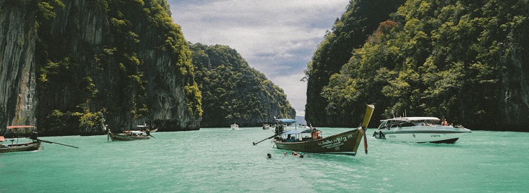 Lagoon with boats surrounded by rocky green hillside in Thailand