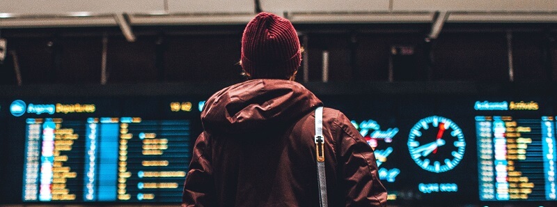 Male wearing beanie and winter jacket looking up at departures boards at the airport