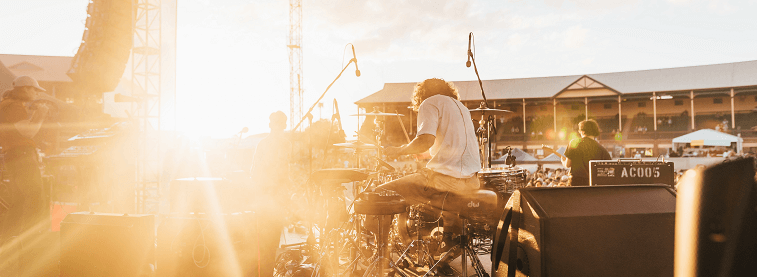 Drummer and band playing music to a crowd with sun in background