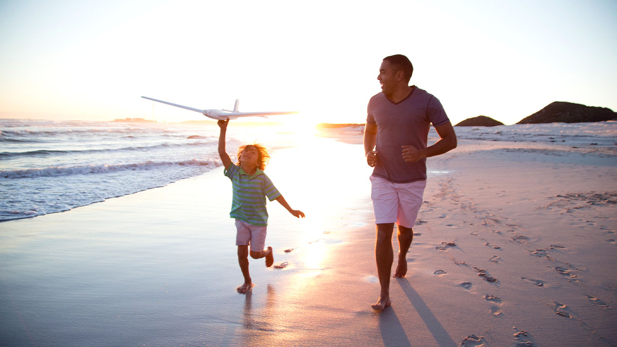 Father and son playing on the beach with a toy plane as the sun starts to set