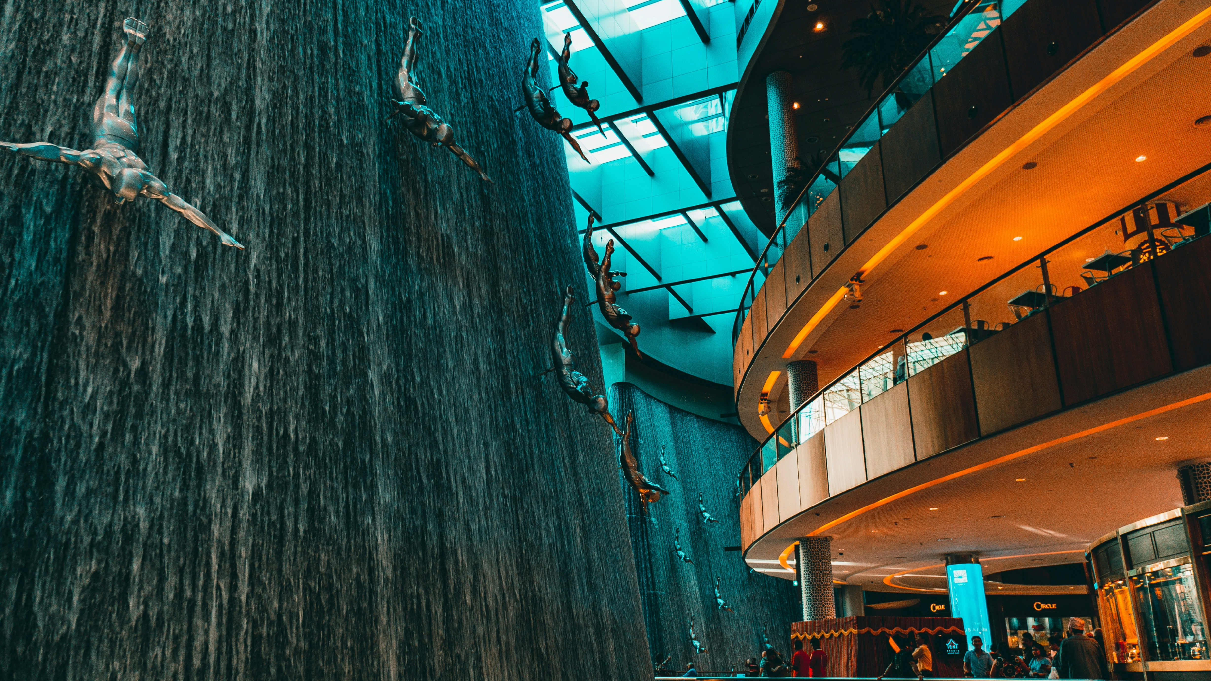 The Dubai Waterfall inside Dubai Mall, with metallic sculptures of divers, set in a multi-level space with glass ceilings and people below