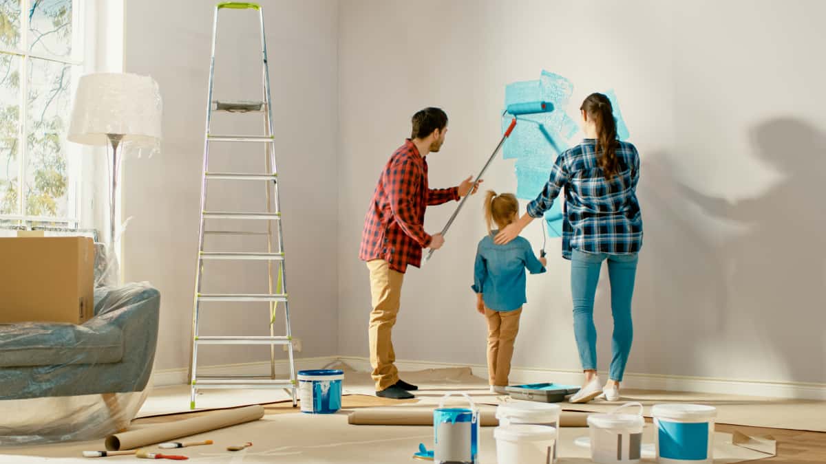Family of 3 doing DIY painting in the home, rolling paint on the walls