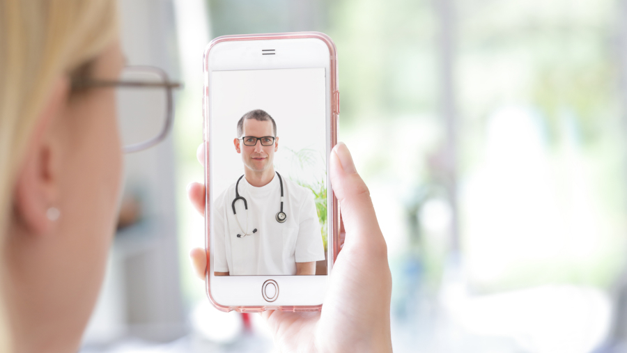 Woman holding her mobile up to her face on a video call with a male doctor looking back at her