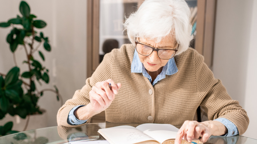 Elderly woman sat at a table in her home filling in a driving licence renewal form