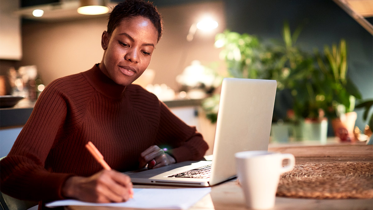 Woman sat at a table in her home with her laptop open in front of her while she fills out a form