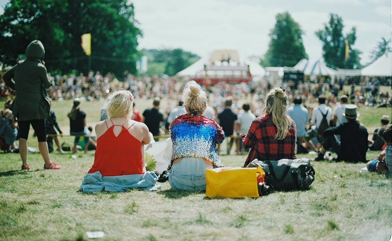 Three women sitting on grass facing towards crowds in the distance