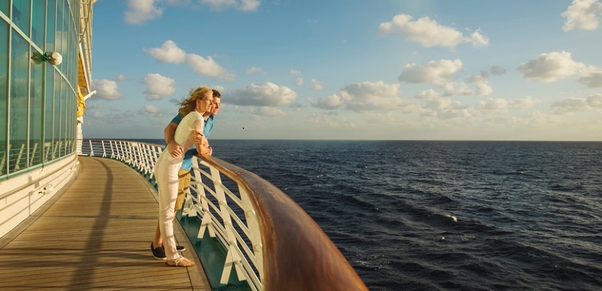 A couple leaning on the railings of a boat, looking out to sea