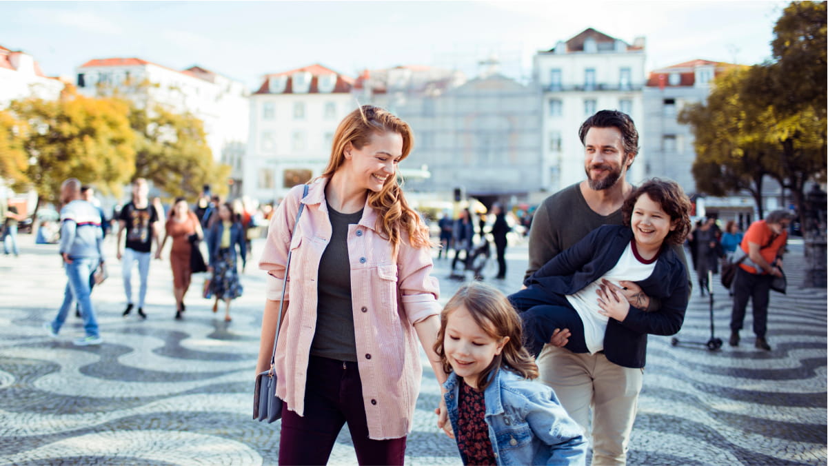 A happy family in a town square, mother her daughter in front of a father carrying his son