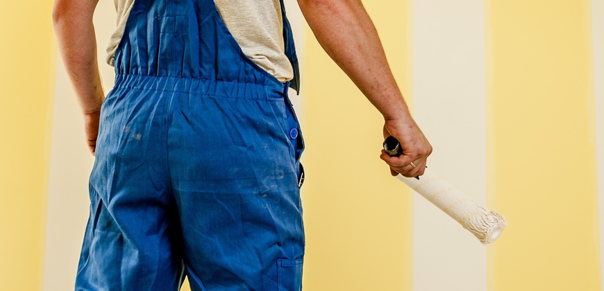 Painter with Painting brush standing in front of a wall with yellow and white strips