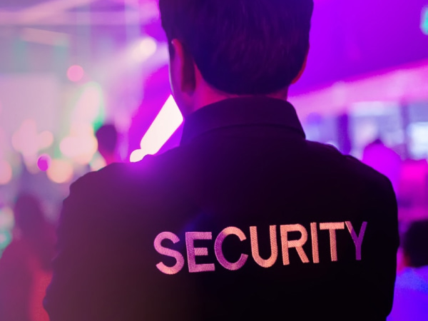 A member of security with his back to us with the word security on his top in a venue setting