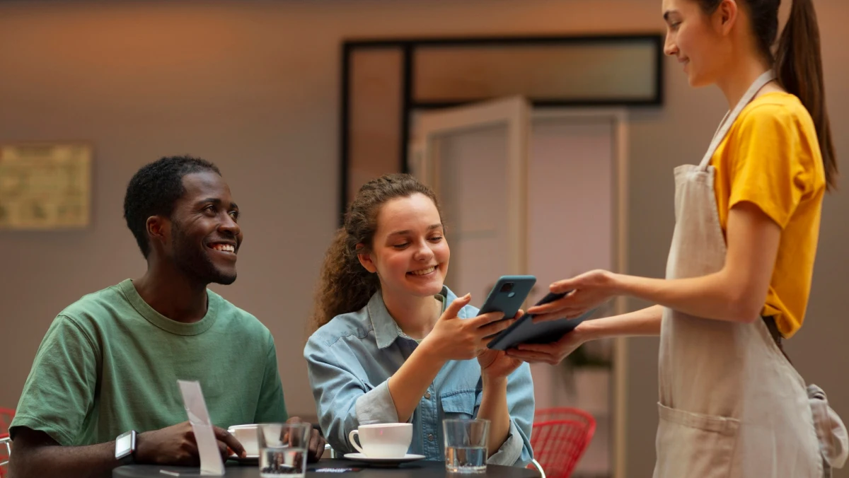 a smiling couple paying with a smartphone at a cafe
