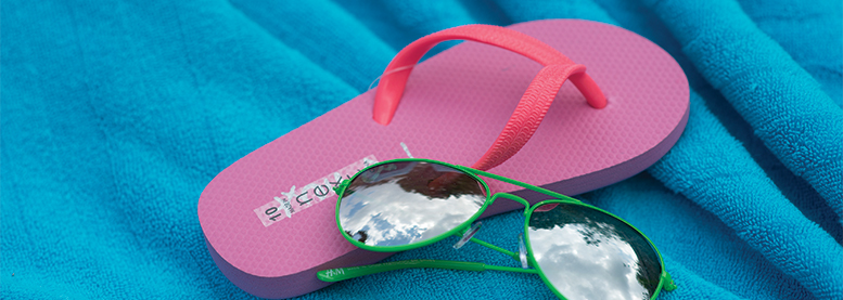 A pair of green sunglasses laid on top of a pink flip flop on top of a blue blanket