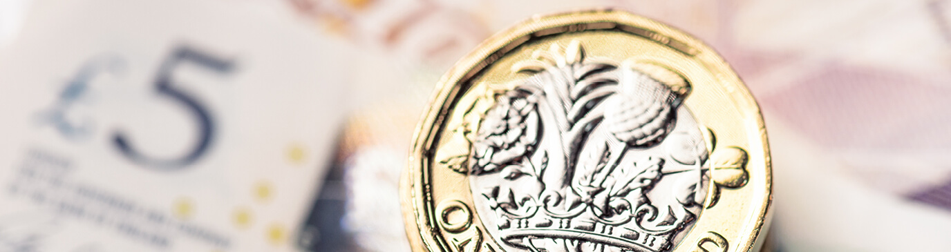 A £5 bank note placed on the left, a British one pound coin, face up on the right