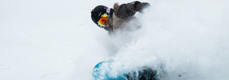 Person snowboarding through snow surrounded with snow spray