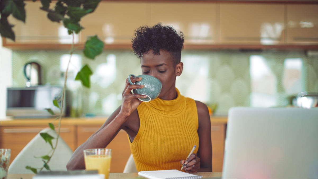 Female sitting down at the table with pen and paper drinking from a mug