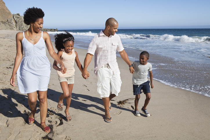Young family of four walking along a sandy beach with waves to their left