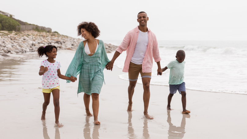 Young family of four walking along a sandy beach with waves to their left