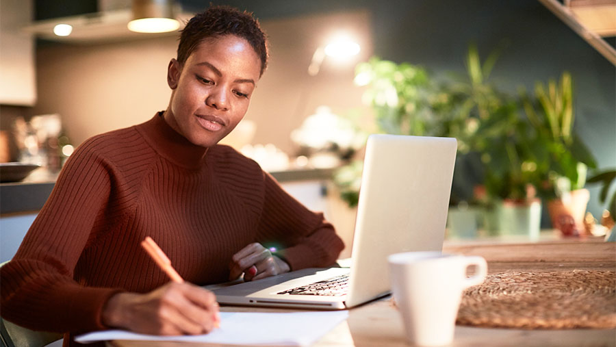 Woman sat at a table in her home with her laptop open in front of her while she fills out a form