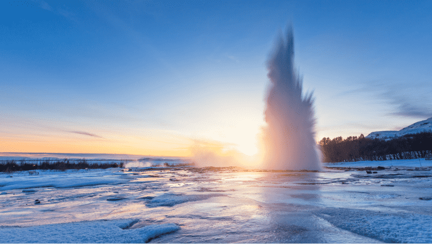 Geysir in Iceland, sun setting in the background surrounded by frozen scenery and trees