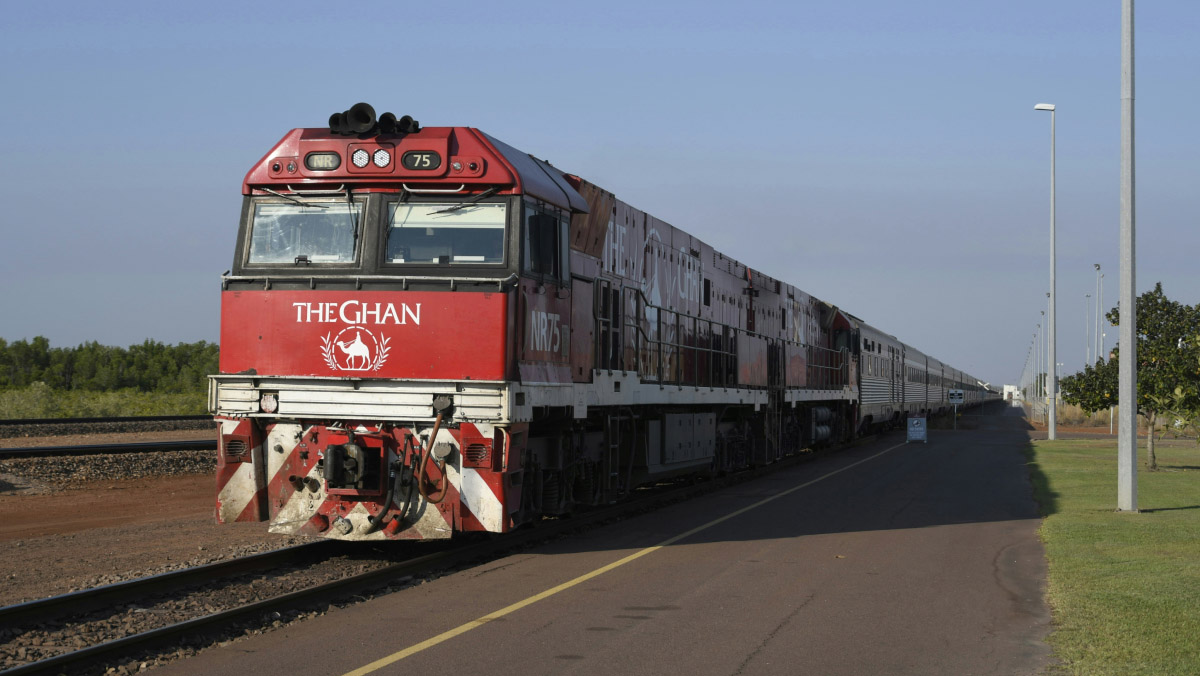 A red and white train travelling down train tracks with the words “The Ghan” on the front of the engine