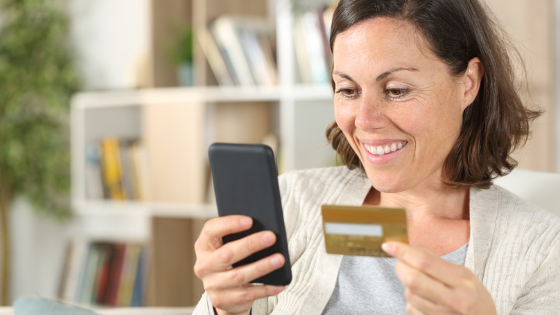 a customer smiling and looking at her phone whilst holding a credit card