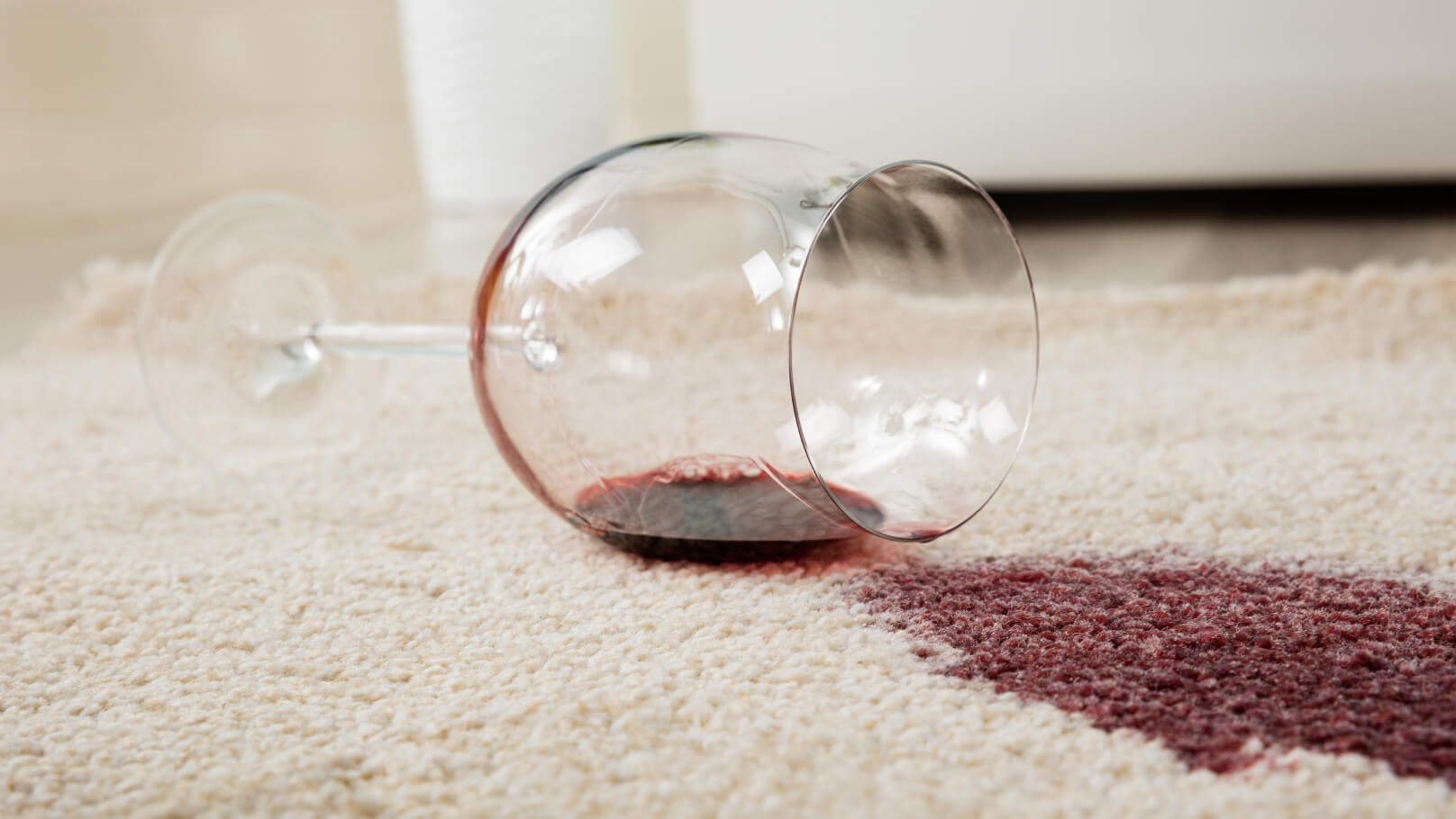 Wine glass on its side with red wine spilling out from the glass on to a white carpet