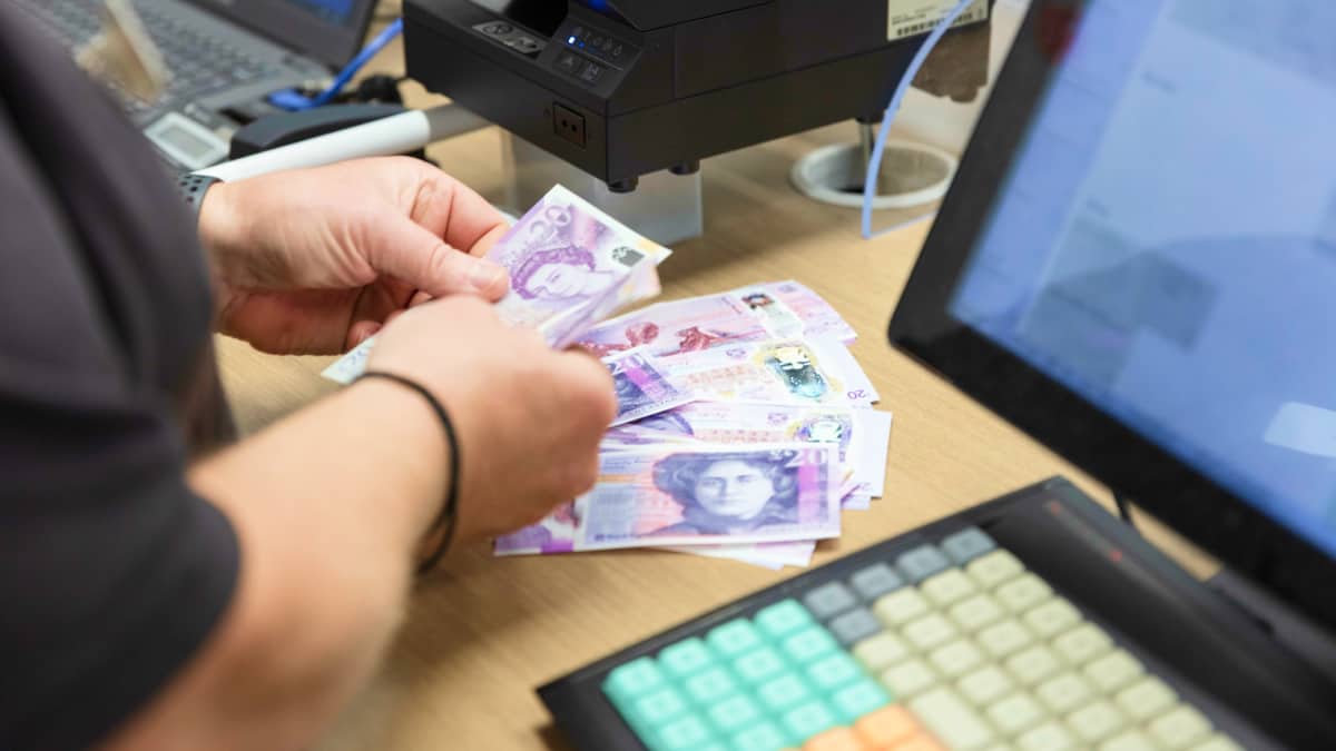 A person in a black shirt, their hands counting money at a post office counter