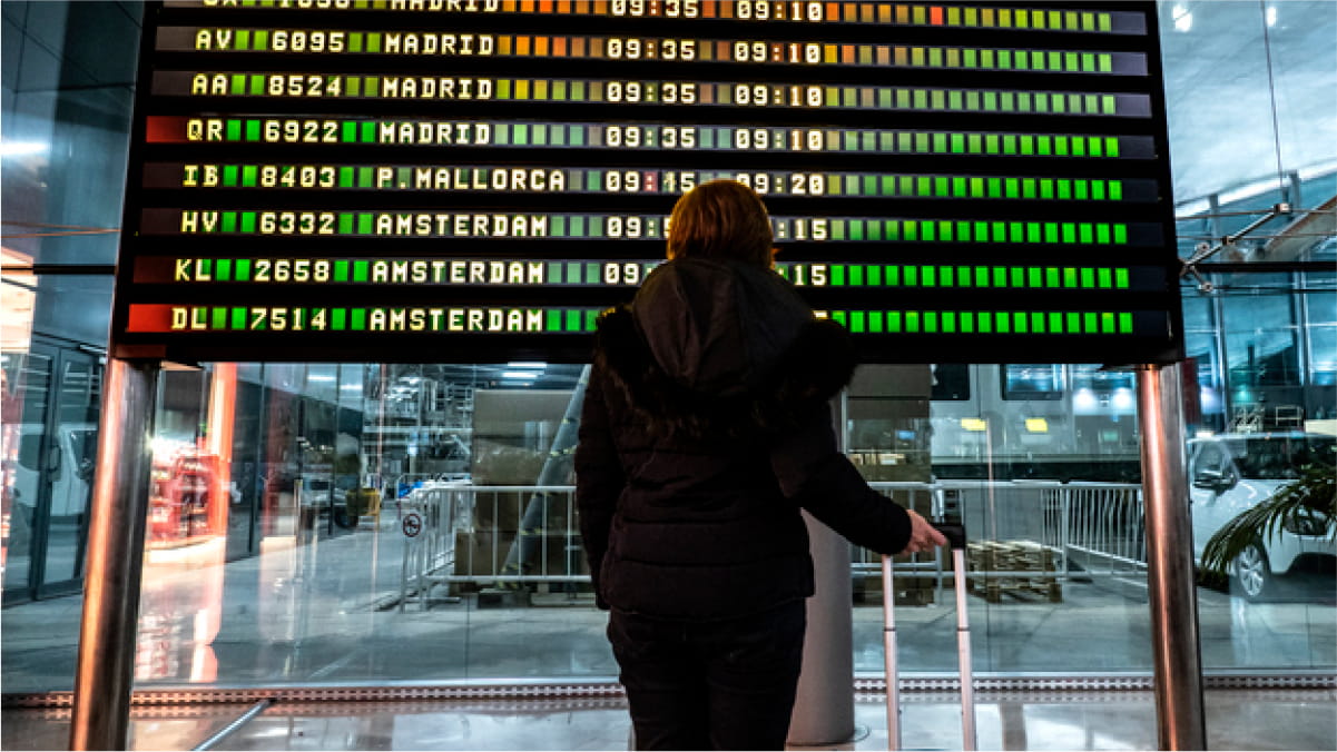 Woman in black autumn clothing, her right hand on suitcase handle looking at flight departures board