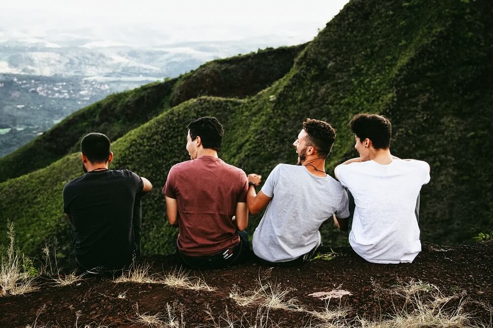 Four young males on hill top laughing and looking at each other with green hillside in distance